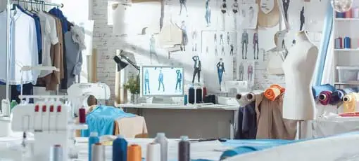 Fashion Designer | Aufnahme eines Sunny Fashion Design Studio. Wir sehen den Arbeitsplatz Personal Computer, Hängekleidung, Nähmaschine und verschiedene Nähartikel auf dem Tisch, Mannequins Stehen, bunte Stoffe.